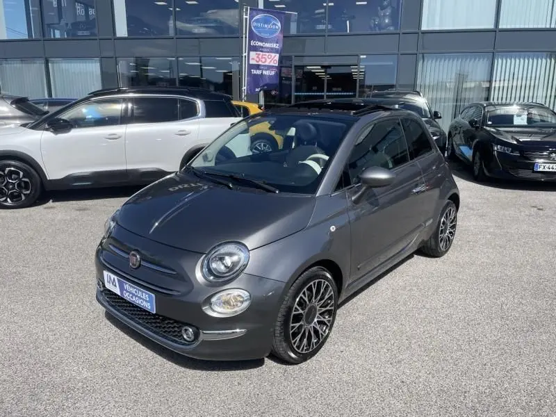 Fiat 500 gris foncé vue 3/4 avant droit, toit ouvrant panoramique et jantes alliage multibranches visibles.