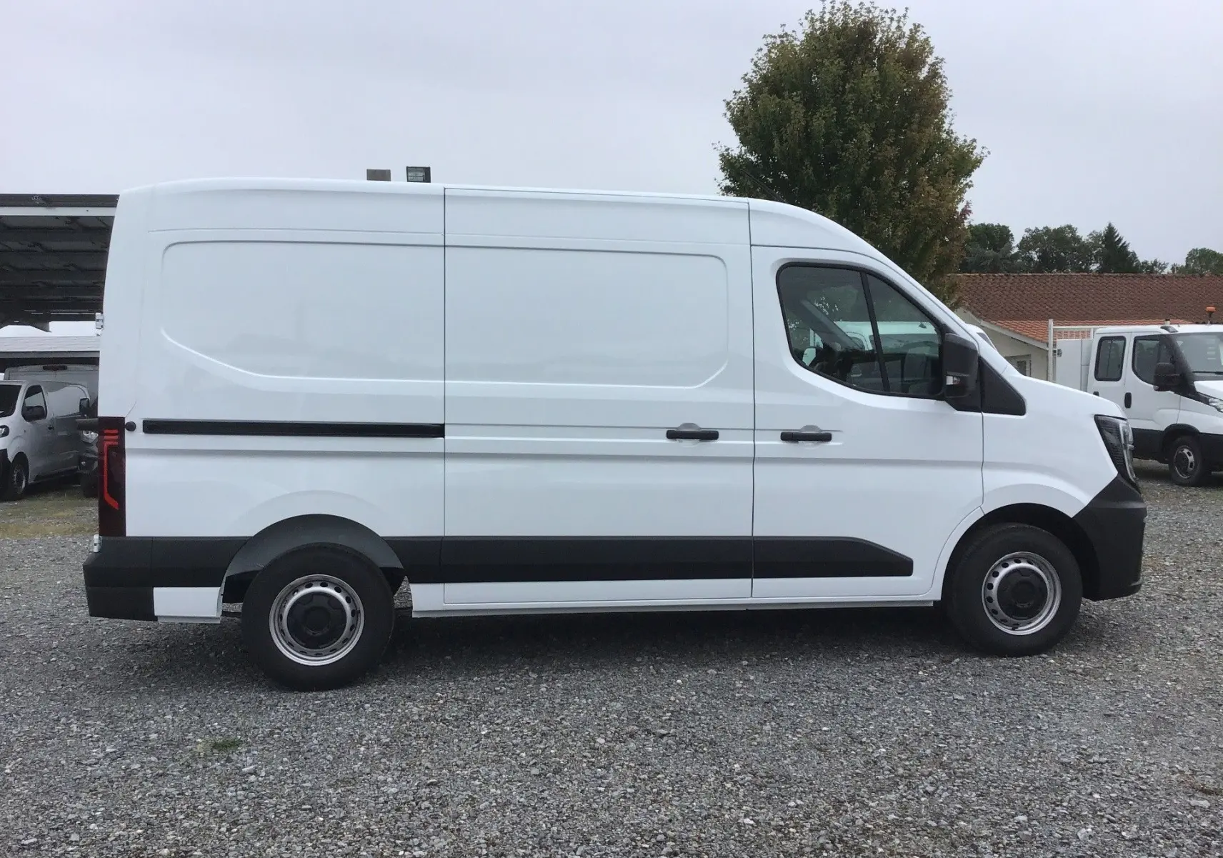 Vue latérale droite d’un utilitaire Renault Master blanc L2H2 avec bande noire et jantes acier sur sol gravillonné.