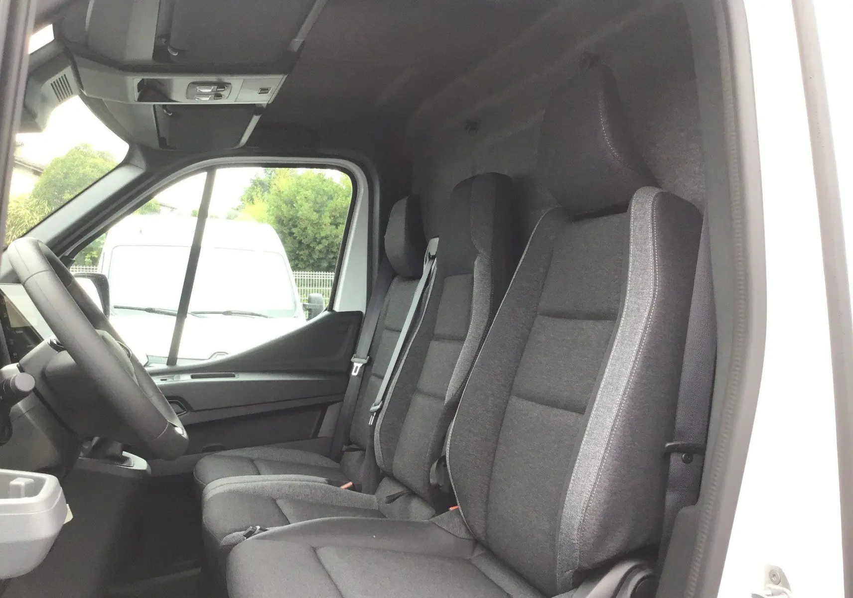 Vue intérieure côté conducteur du Renault Master blanc, montrant les trois sièges avant en tissu gris foncé.