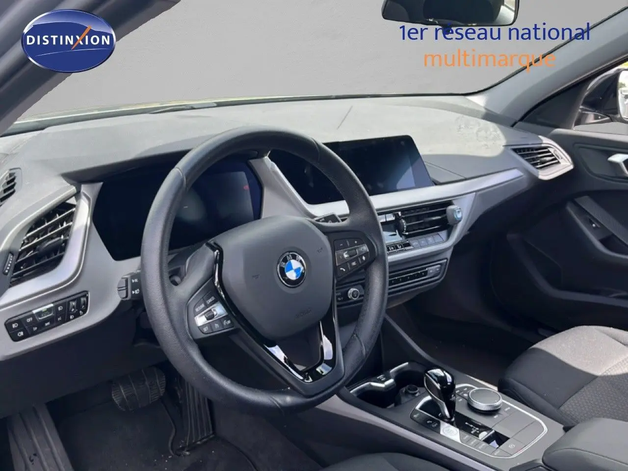 Intérieur BMW Série 1 116i 2022 vu côté conducteur, volant cuir noir et tableau de bord moderne gris foncé.
