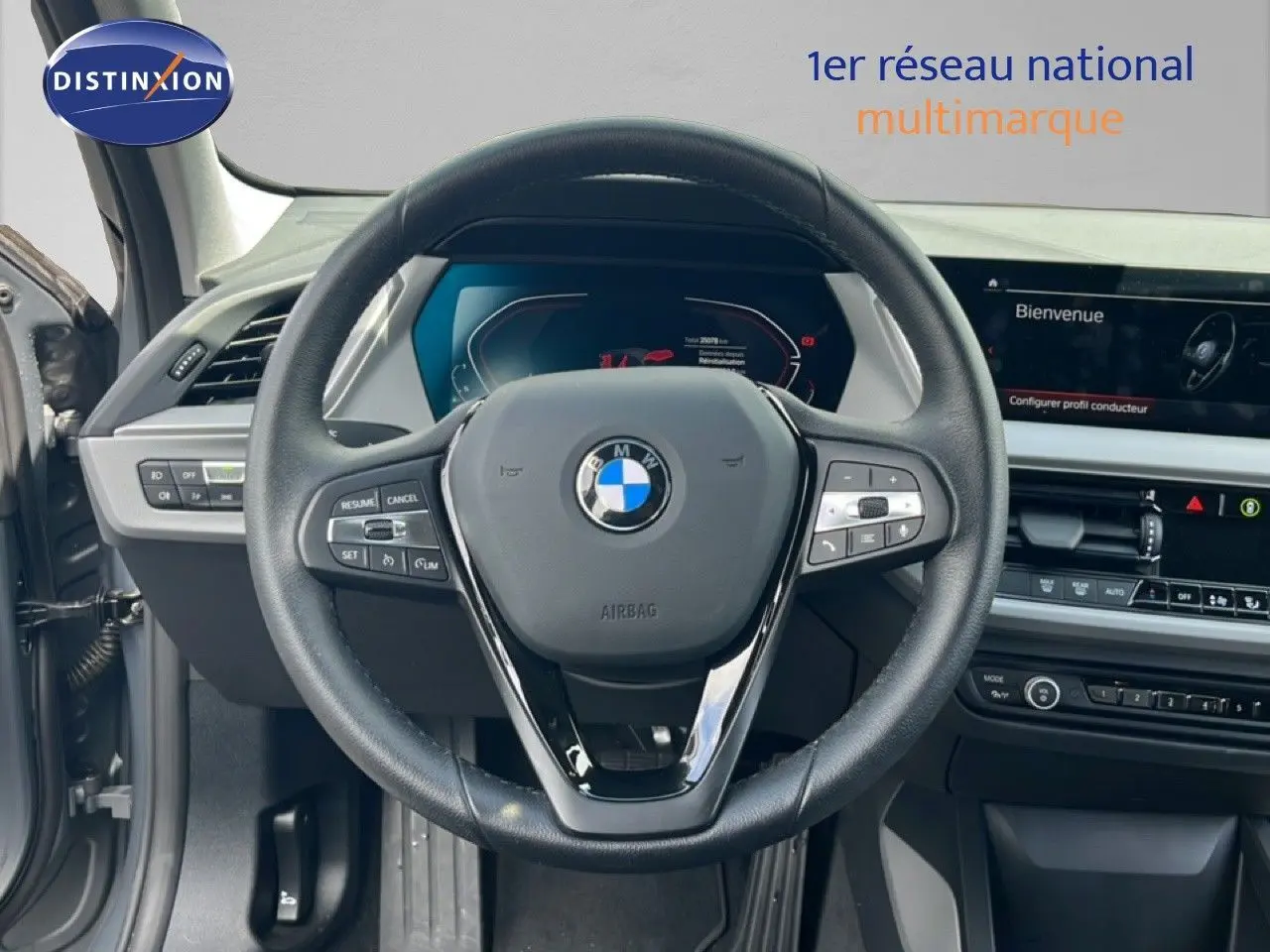 Vue intérieure centrée sur le volant noir d’une BMW Série 1 116i 2022 avec tableau de bord numérique et écran tactile.