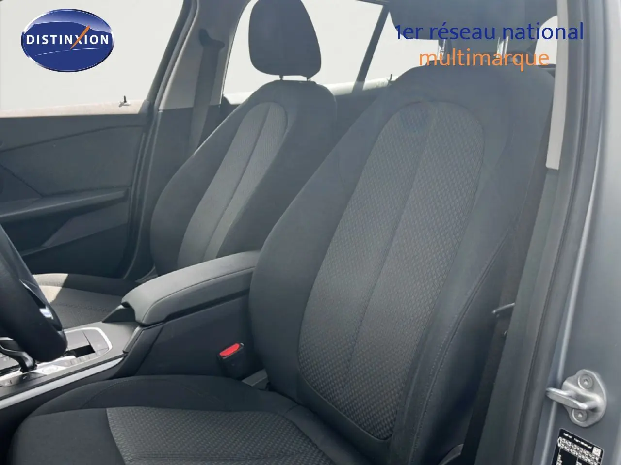 Vue intérieure côté conducteur de la BMW Série 1 116i 2022 avec sièges tissu gris foncé et accoudoir central.