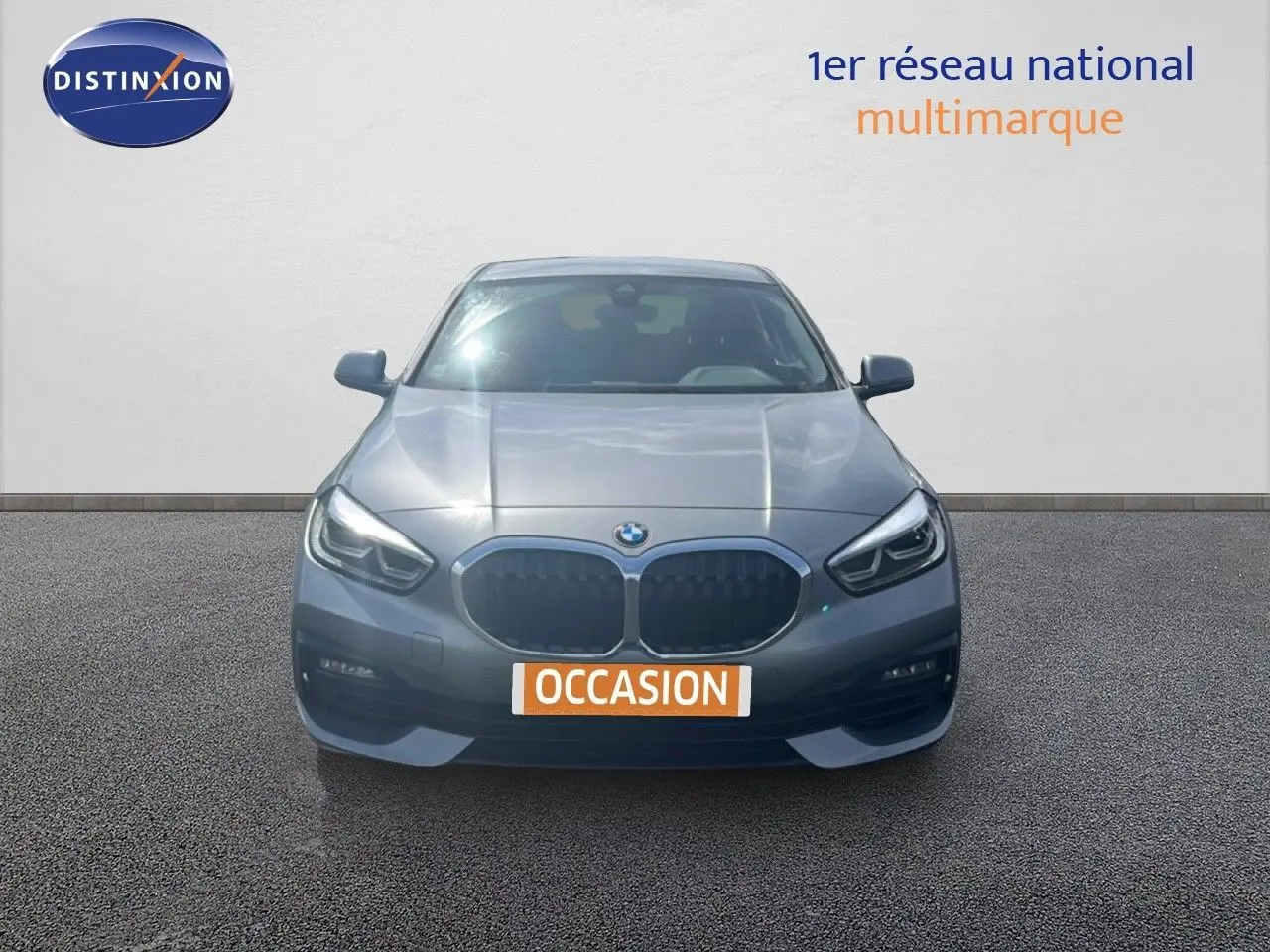 BMW Série 1 116i gris Frozen Pure Grey vue de face, avec calandre double haricot et phares LED allumés.
