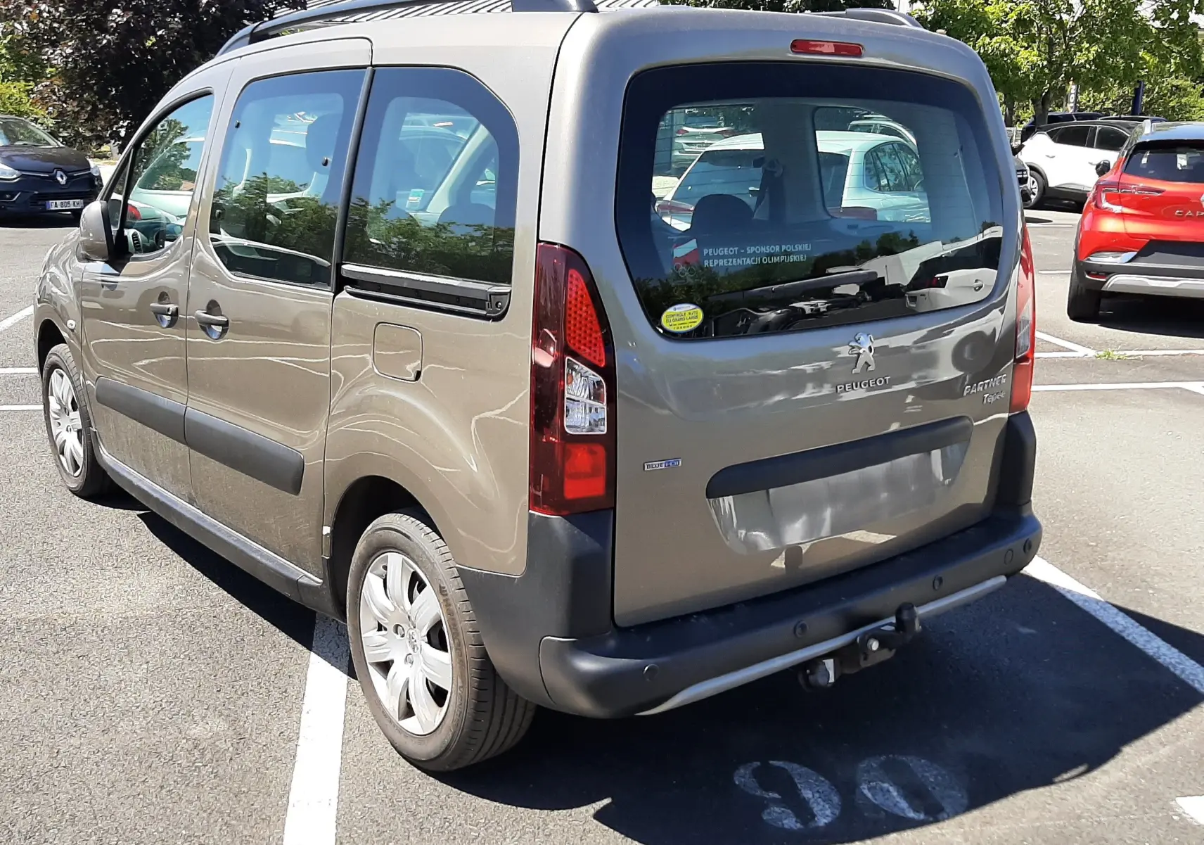 Vue 3/4 arrière droite d'un Peugeot Partner Tepee marron 2016 avec attelage et vitres teintées, stationné en extérieur.