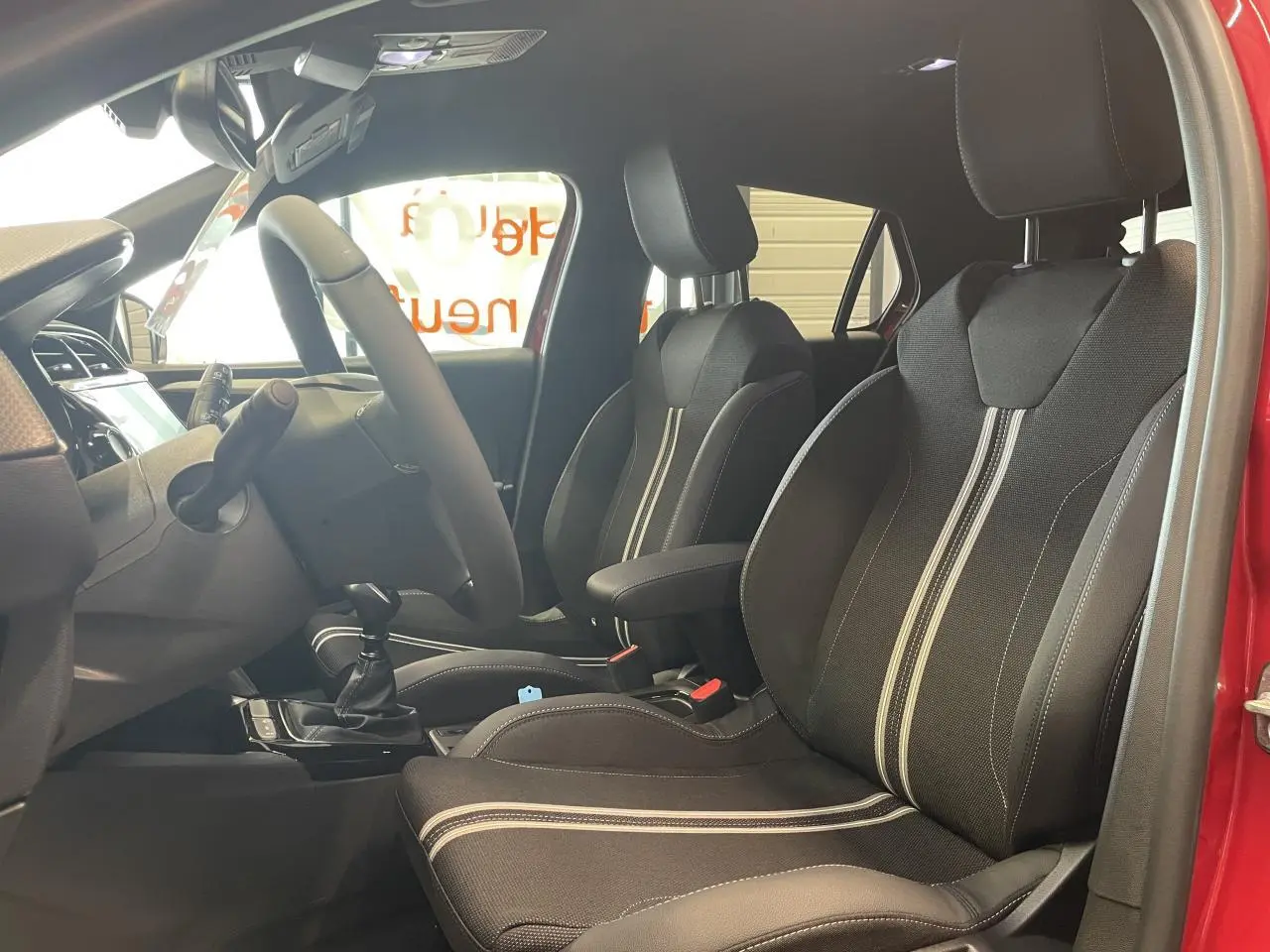 Vue intérieure côté conducteur de l'Opel Corsa rouge 2026, sièges sport noirs avec bandes blanches et volant cuir.