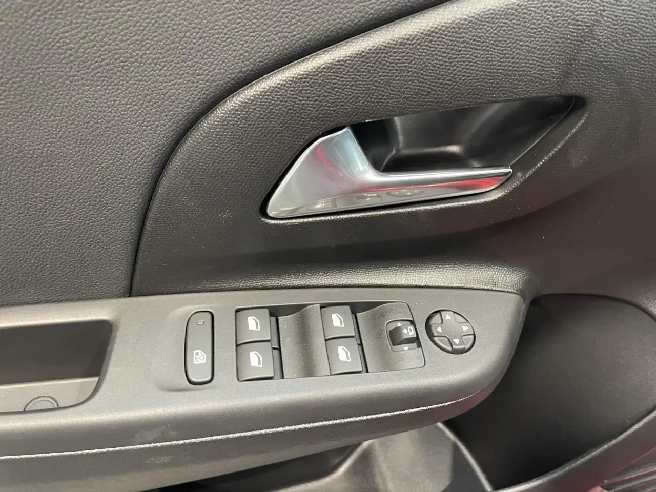 Détail de la porte côté conducteur de l’Opel Corsa rouge montrant les commandes électriques des vitres et rétroviseurs.