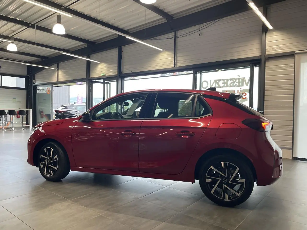Opel Corsa rouge vue de profil côté gauche, avec jantes alliage et toit noir en showroom lumineux.