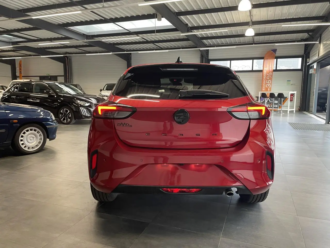 Vue arrière d'une Opel Corsa rouge métallisée avec feux LED allumés dans un showroom.