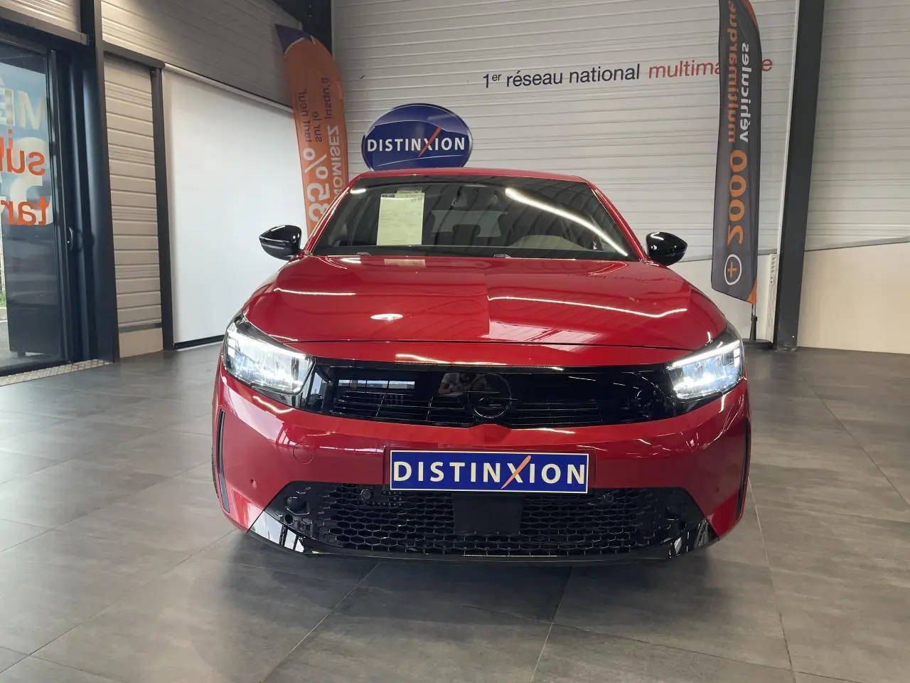 Vue avant d'une Opel Corsa rouge 2026 avec calandre noire et phares LED allumés en showroom.