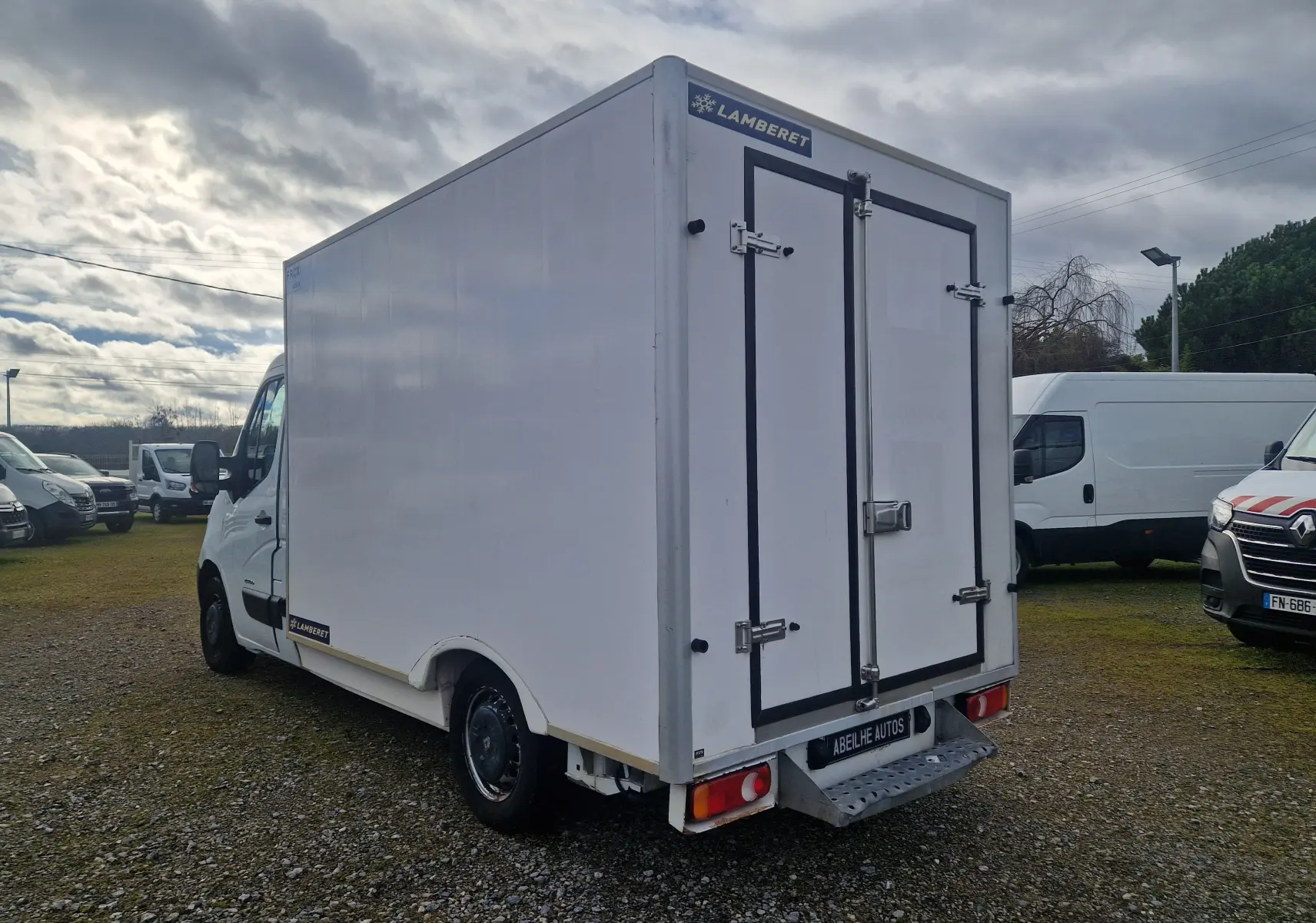Vue 3/4 arrière droite d’un Renault Master blanc avec cellule frigorifique Lamberet et marchepied arrière sur un terrain extérieur.