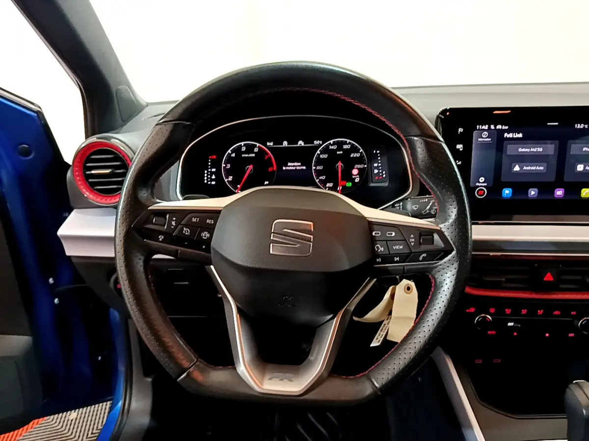 Volant cuir perforé avec surpiqûres rouges et tableau de bord numérique du SEAT Arona bleu, vue intérieure frontale.