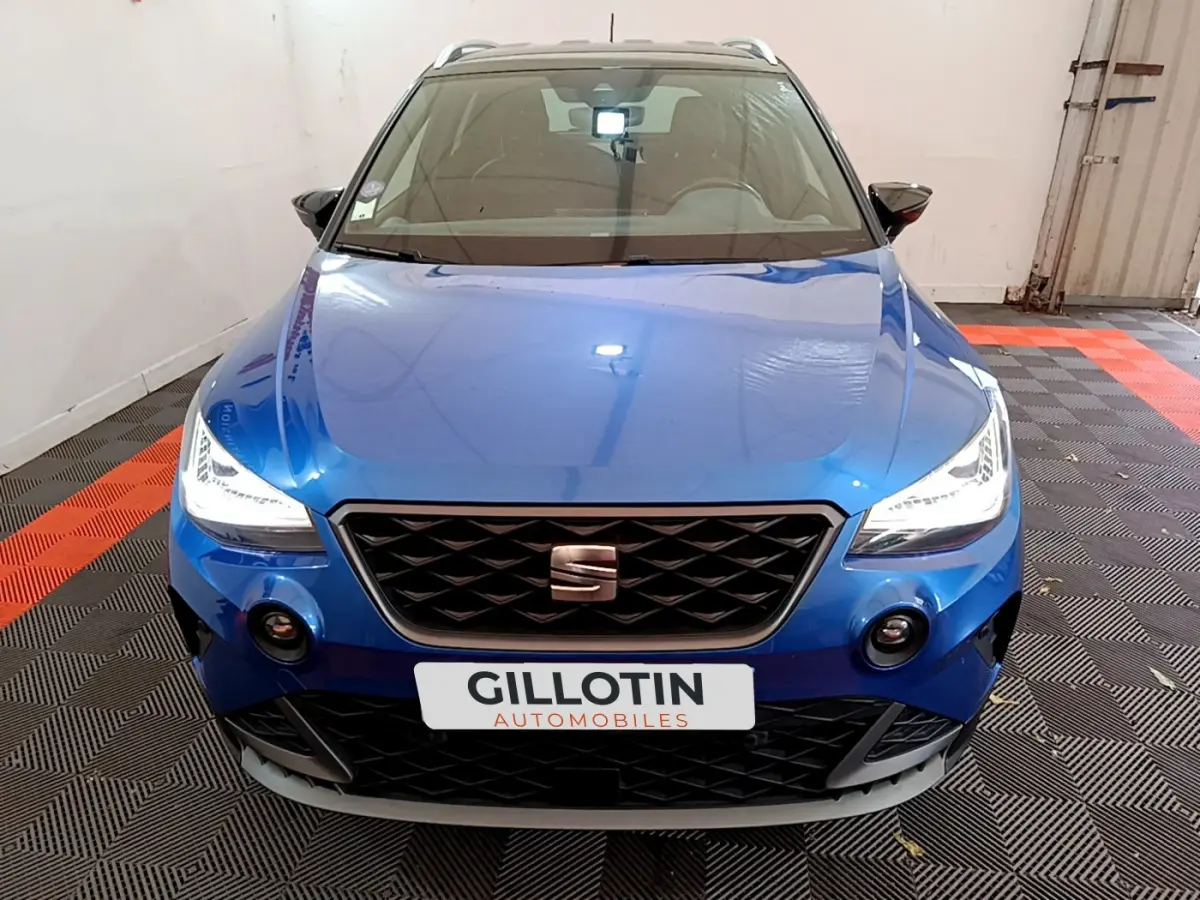 Vue frontale d'un SEAT Arona bleu 2022 avec phares LED allumés et calandre noire distinctive.