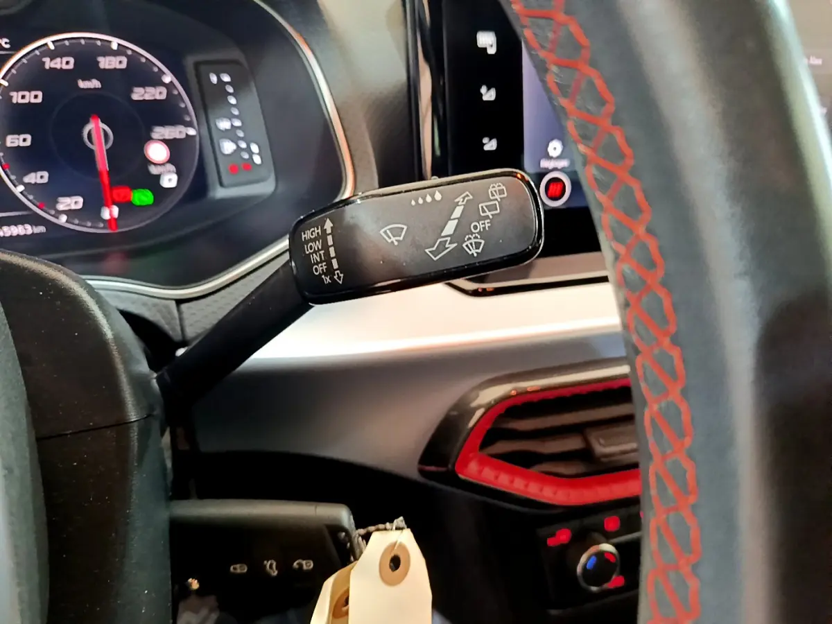 Gros plan sur la commande d’essuie-glace du tableau de bord d’un SEAT Arona bleu, volant cuir noir avec surpiqûres rouges.