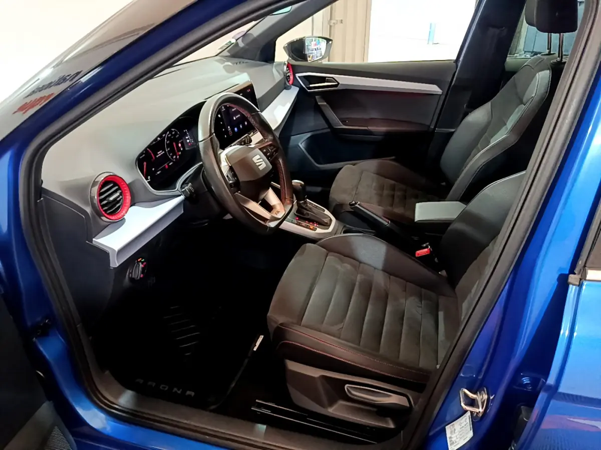 Vue intérieure côté conducteur du SEAT Arona bleu 2022, montrant sièges noirs, volant cuir et tableau de bord digital.