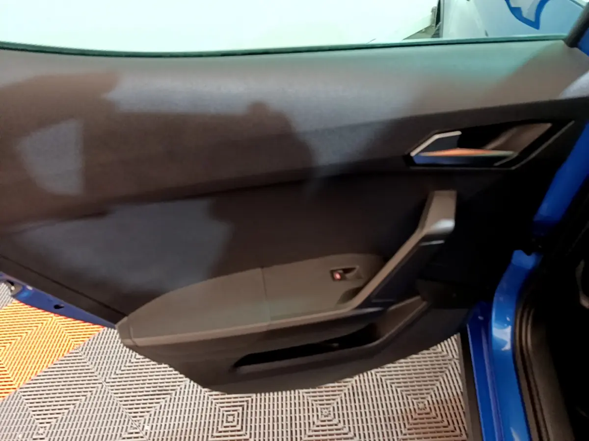 Intérieur de la porte côté gauche d'une SEAT Arona bleu 2022, avec poignée et panneau de commande noir.
