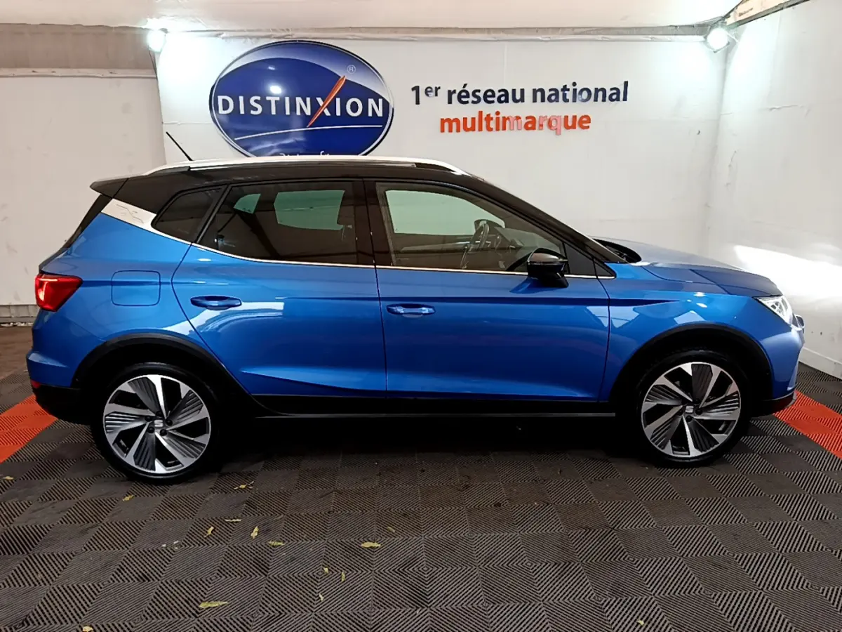 Profil côté gauche d'un SUV SEAT Arona bleu 2022 avec toit blanc et jantes alliage distinctives dans un showroom.