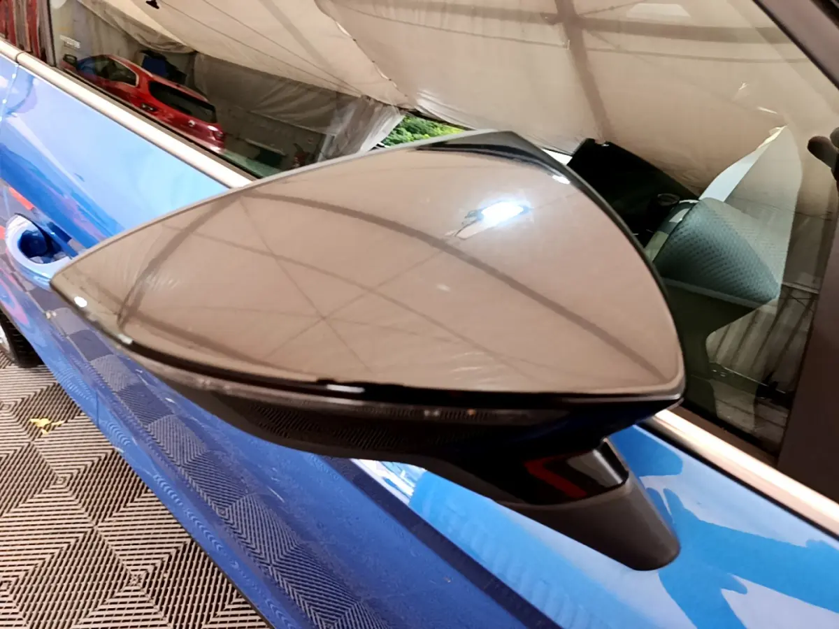 Rétroviseur droit noir brillant sur porte bleue d'une SEAT Arona 2022 vue en gros plan intérieur garage.