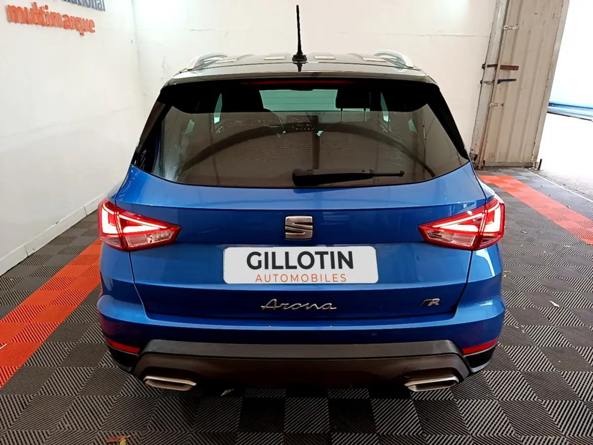 Vue arrière d'un SEAT Arona bleu 2022 finition FR avec feux LED et double sortie d'échappement dans un garage.