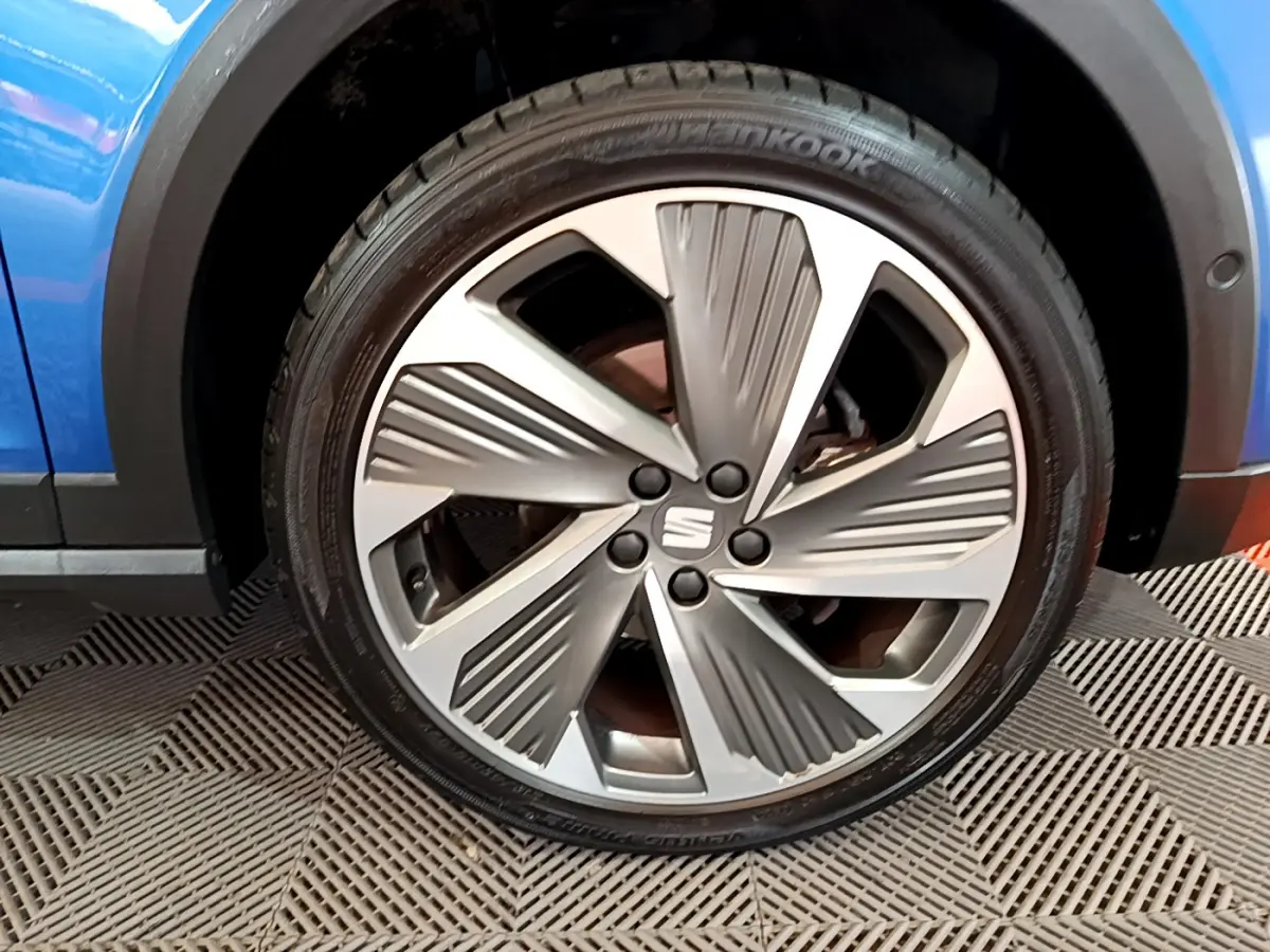 Gros plan sur la jante avant droite du SEAT Arona bleu 2022, avec logo central et design à cinq branches stylisées.