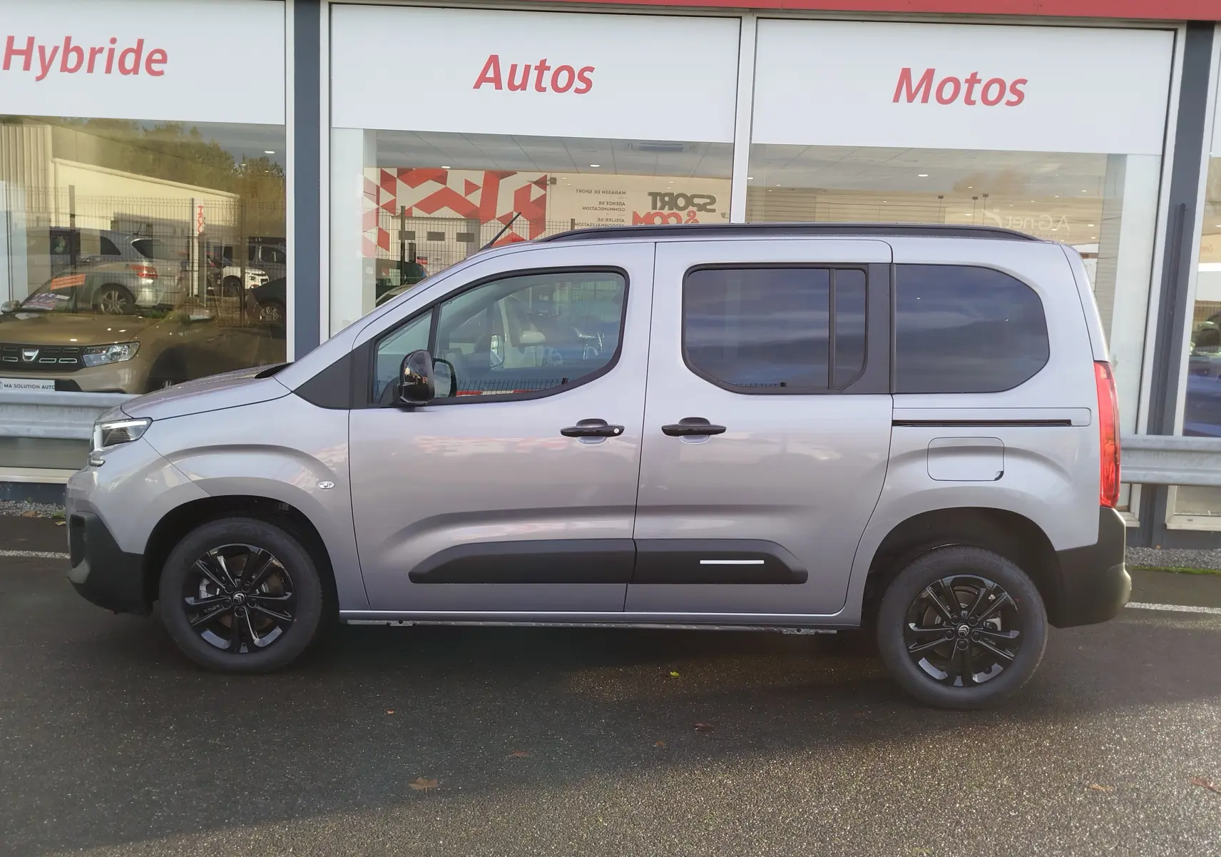 Profil droit d'un Citroën Berlingo gris acier 2026 avec vitres teintées et jantes noires devant un showroom.