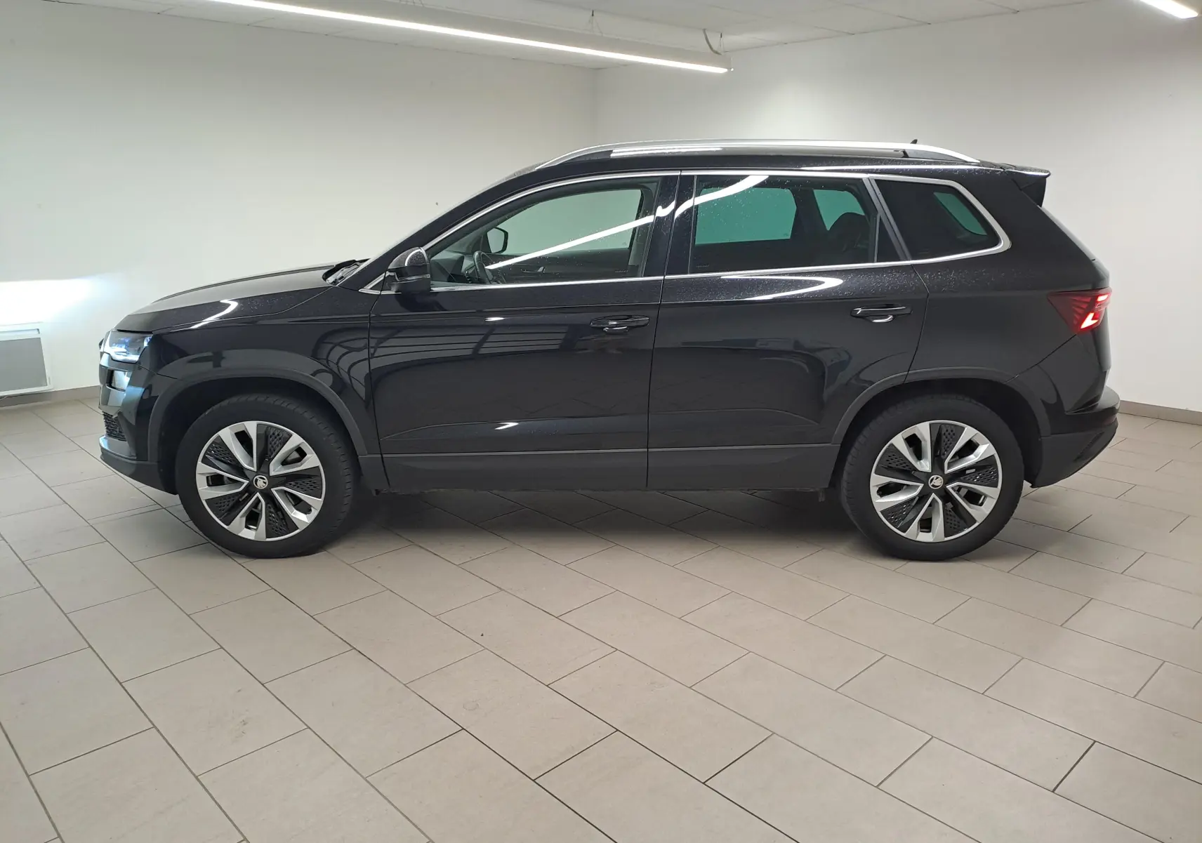 Vue latérale droite d'un Skoda Karoq 2023 noir Magic Nacré, avec jantes alliage et feux arrière allumés.