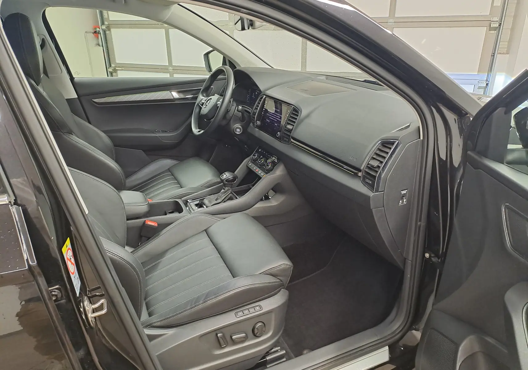 Vue intérieure côté conducteur du Skoda Karoq noir Magic Nacré 2023, avec sellerie cuir et tableau de bord moderne.