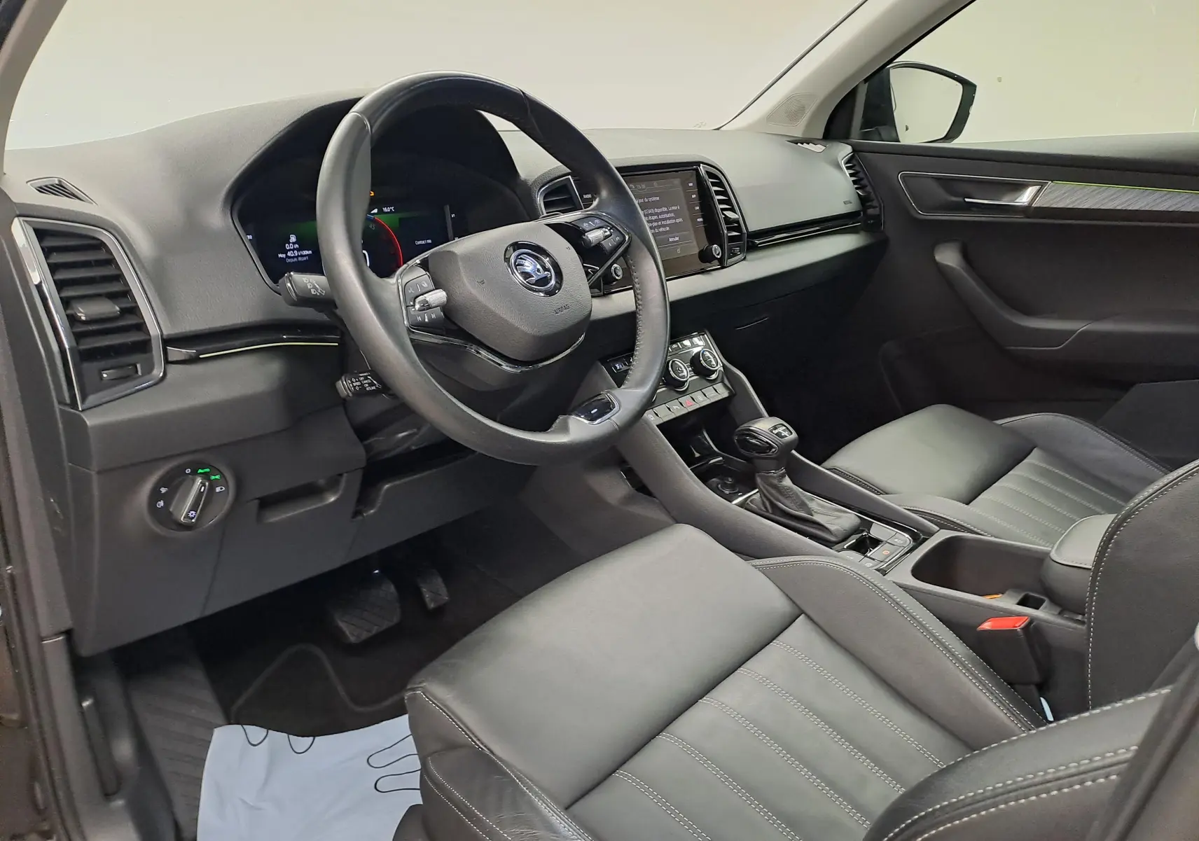 Vue intérieure côté conducteur du Skoda Karoq 2023, sellerie cuir noire et tableau de bord moderne avec écran tactile.