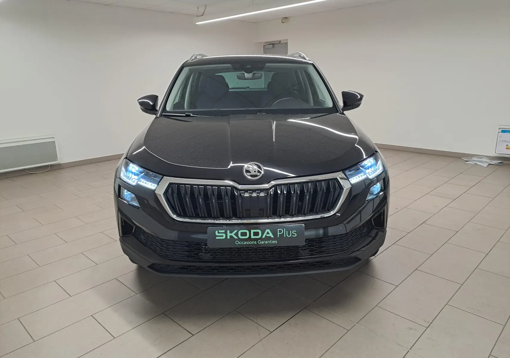Vue frontale d'un Skoda Karoq 2023 noir Magic Nacré avec phares LED allumés dans un showroom.