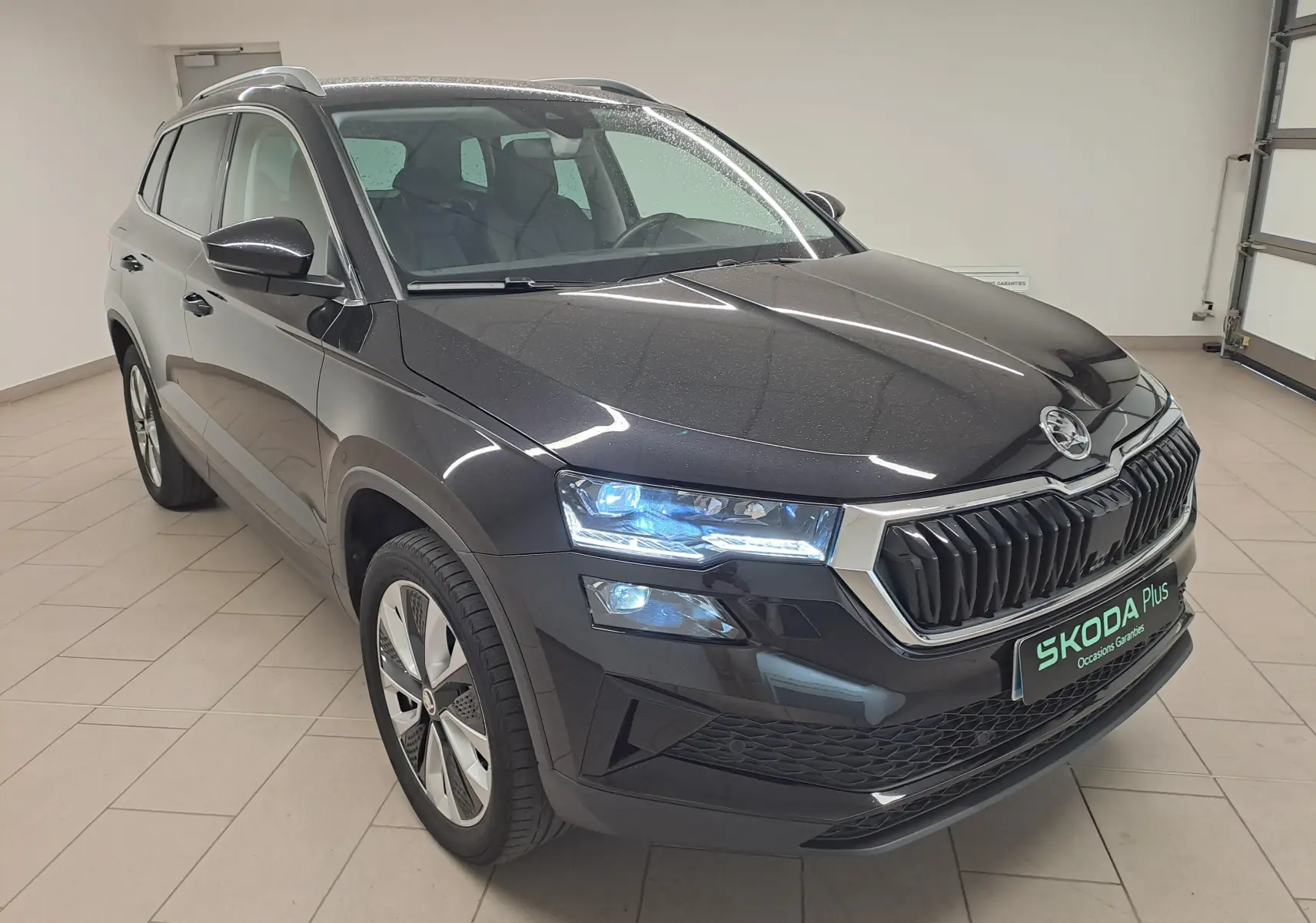 Vue 3/4 avant du Skoda Karoq noir Magic Nacré 2023 avec phares allumés et calandre chromée distinctive.
