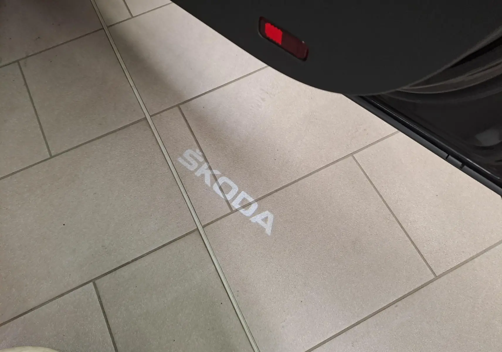 Projection lumineuse du logo SKODA au sol depuis la porte ouverte d’un SUV noir Magic Nacré, vue intérieure côté droit.