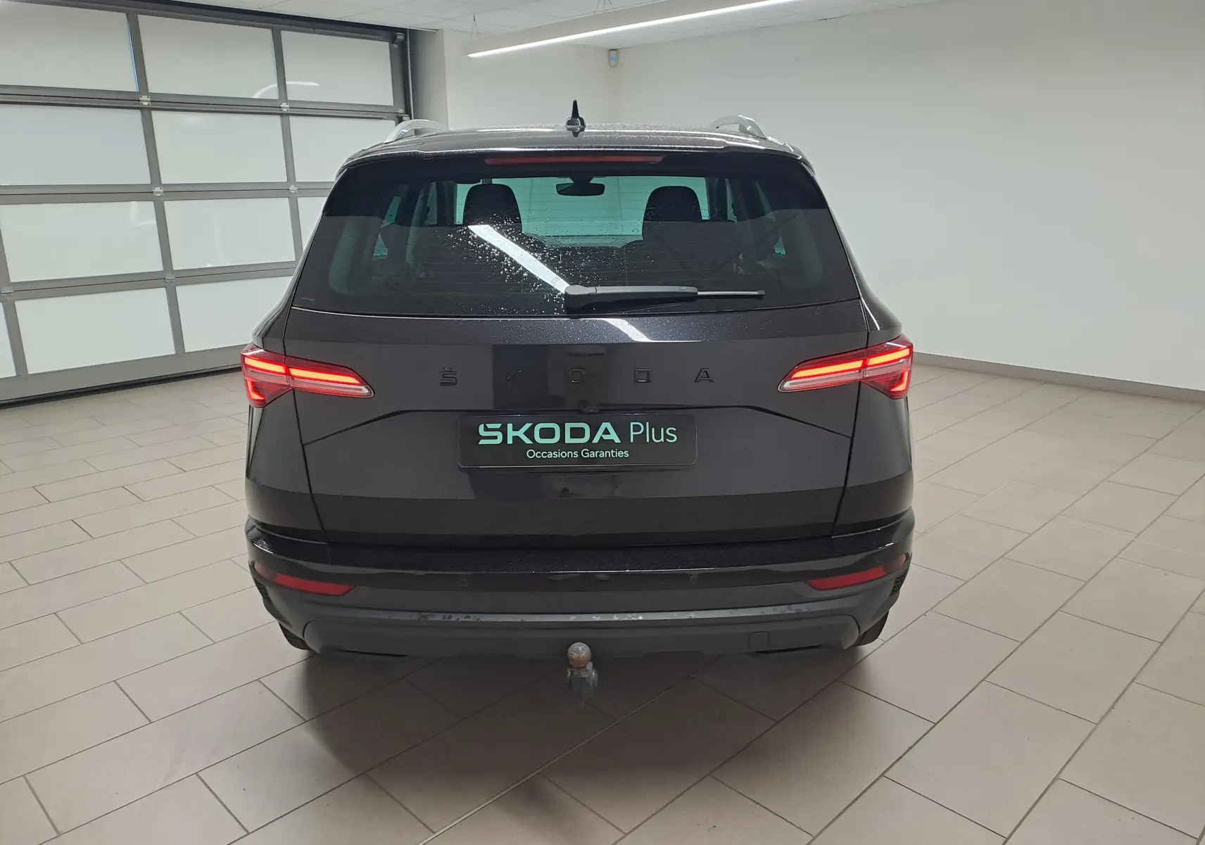 Vue arrière d'un Skoda Karoq noir Magic Nacré 2023 avec feux allumés et crochet d'attelage escamotable visible.