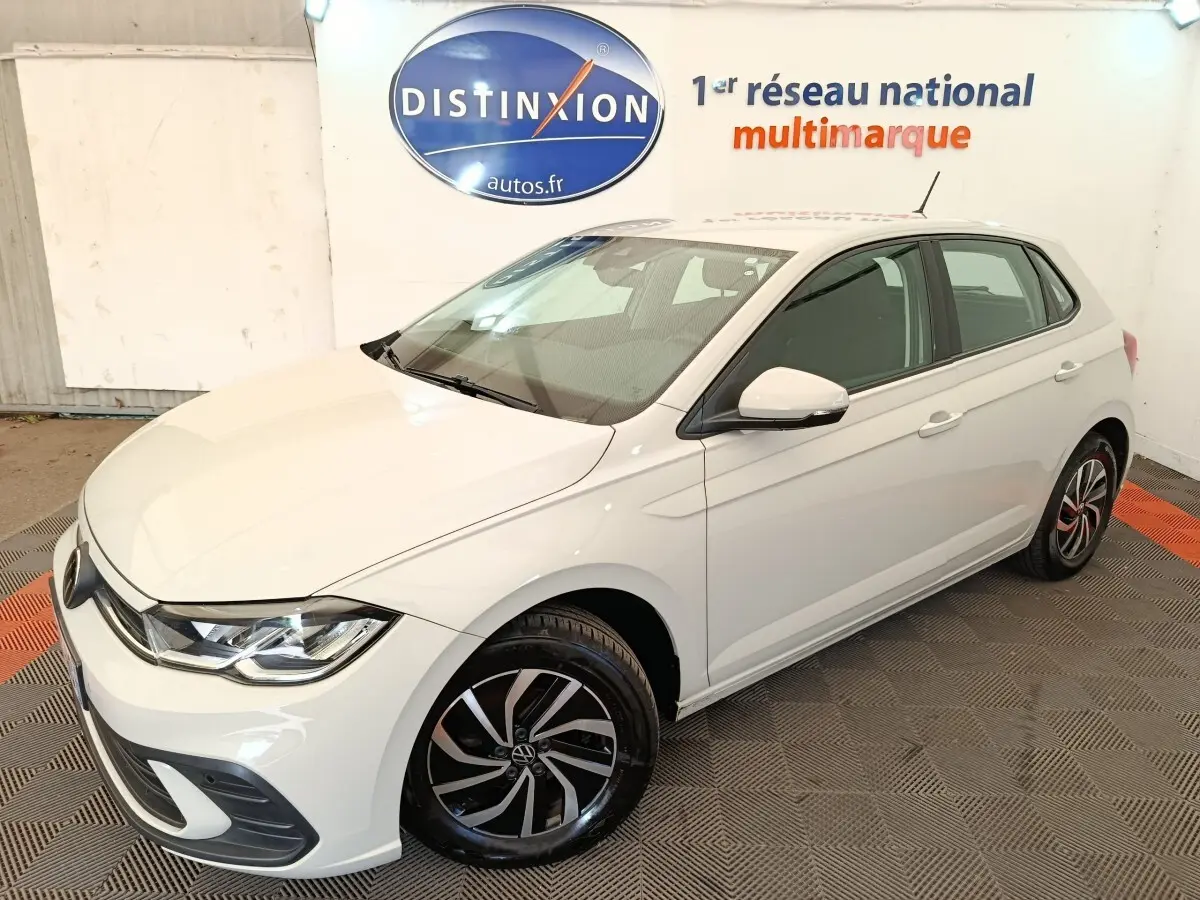 Vue 3/4 avant droite d'une Volkswagen Polo blanche avec jantes alliage noires et détails chromés dans un showroom.