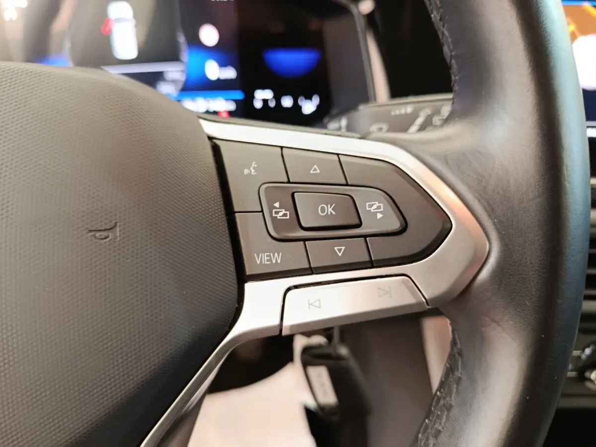 Gros plan sur le volant cuir et alu multifonctions de la Volkswagen Polo gris clair, avec commandes intégrées et affichage numérique en arrière-plan.
