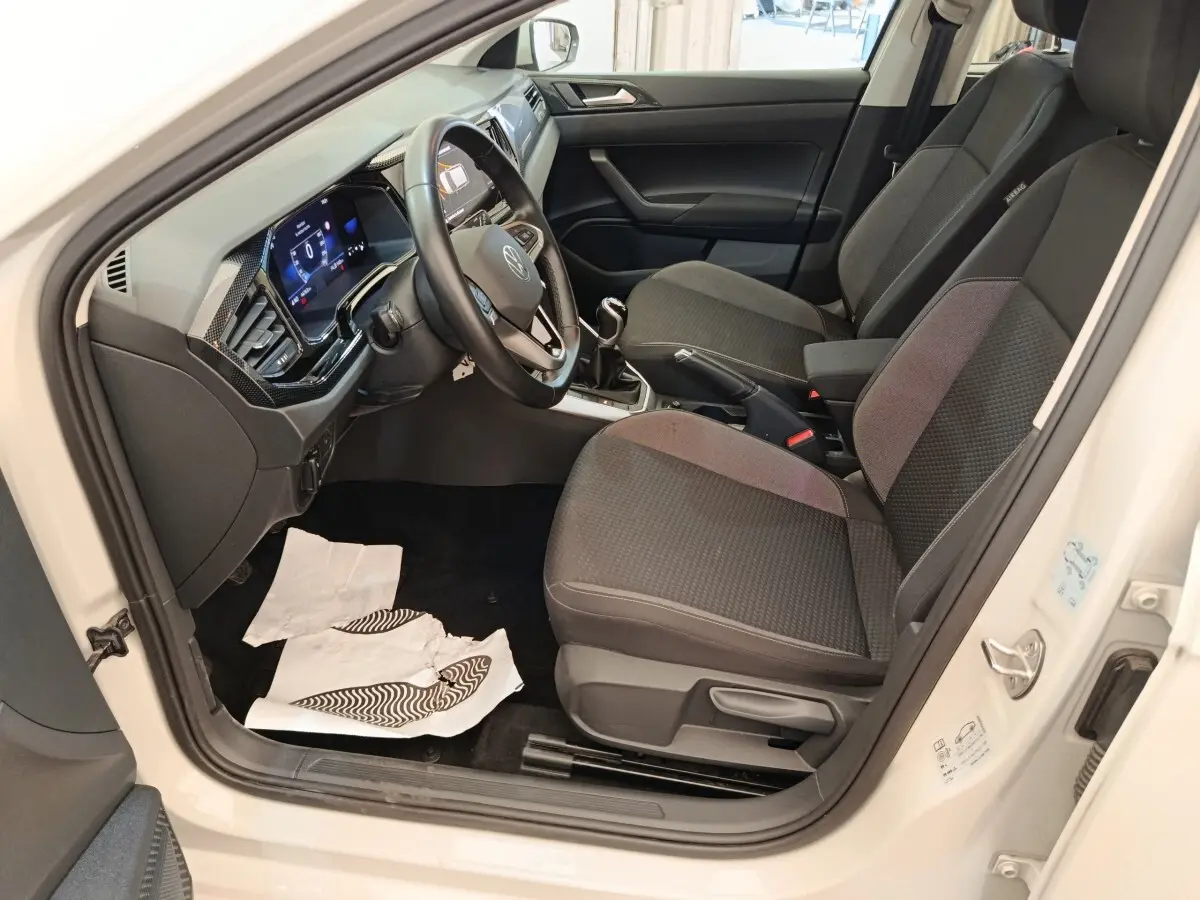 Vue intérieure côté conducteur de la Volkswagen Polo gris clair 2023, montrant le volant multifonctions et les sièges tissu noirs.