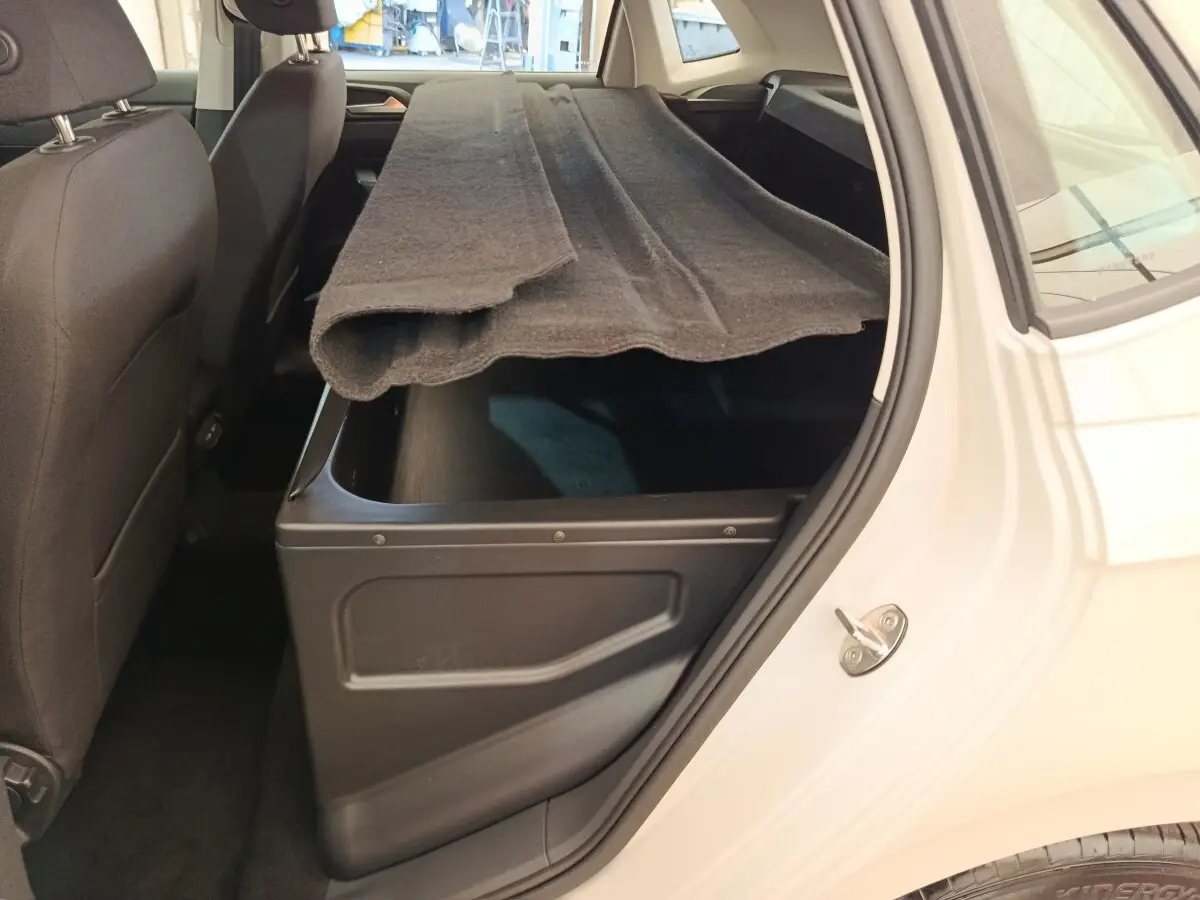 Vue intérieure côté droit du coffre ouvert d'une Volkswagen Polo gris clair avec tapis de coffre partiellement replié.