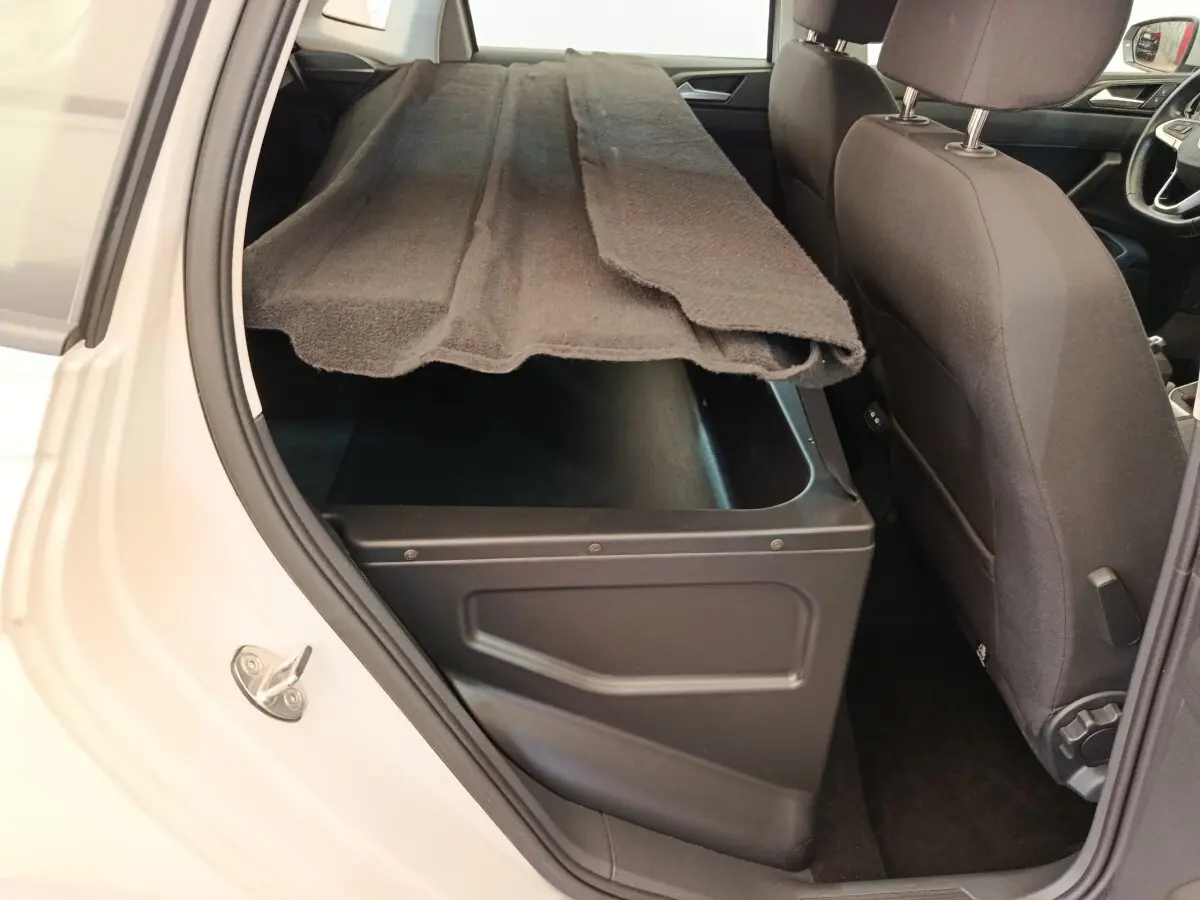 Vue intérieure côté arrière droit d'une Volkswagen Polo 2023 gris clair avec coffre de rangement sous la banquette arrière.