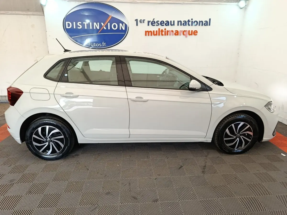 Vue latérale droite d'une Volkswagen Polo gris clair 2023 avec jantes alliage noires et blanches, en intérieur showroom.