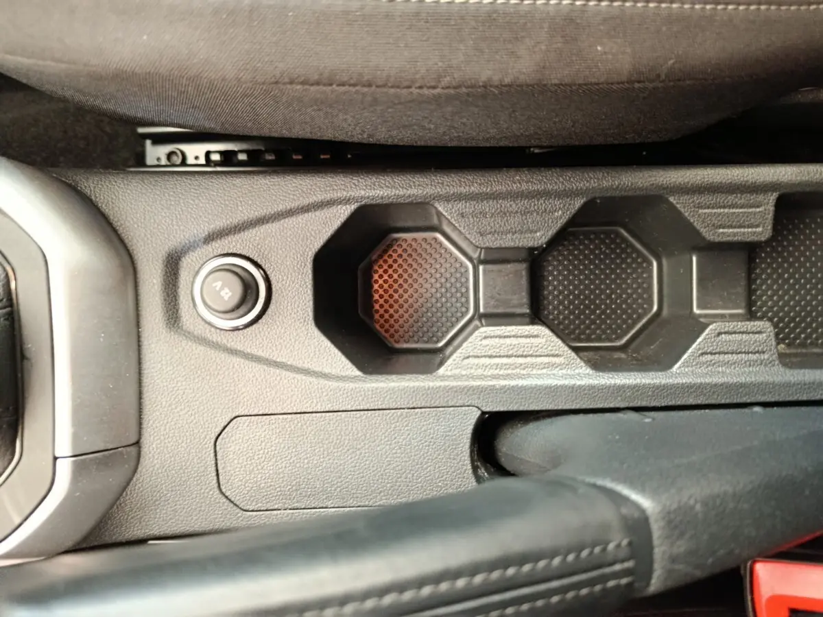 Gros plan sur la console centrale noire de la Volkswagen Polo 2023, montrant le bouton 12V et le frein à main cuir.