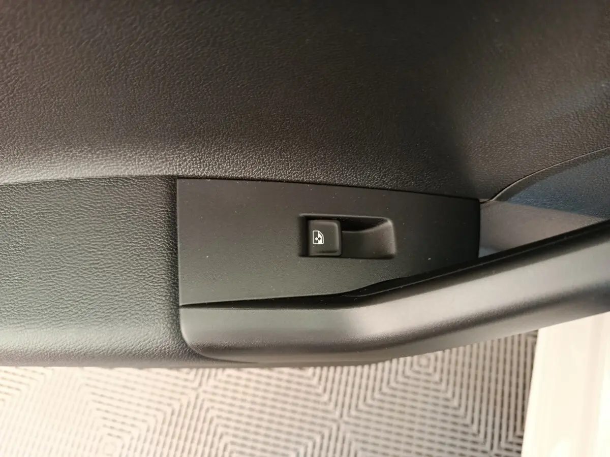 Gros plan sur le bouton de commande de la vitre électrique côté conducteur d'une Volkswagen Polo gris clair.