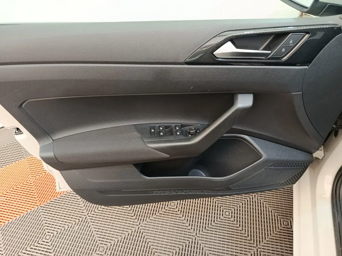 Vue intérieure côté gauche de la porte avant d'une Volkswagen Polo 2023, avec commandes électriques et poignée noire.
