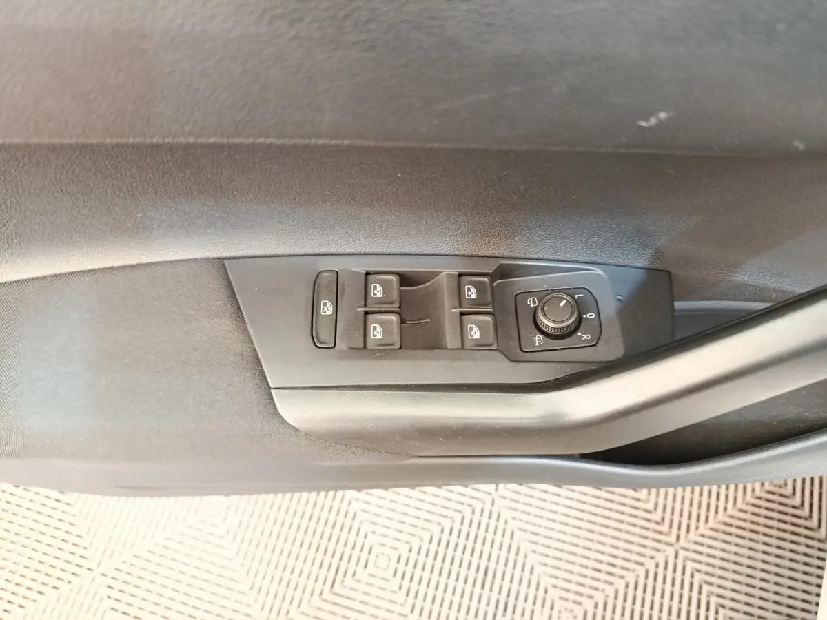 Gros plan sur les commandes des vitres et rétroviseurs électriques côté conducteur d'une Volkswagen Polo gris clair.