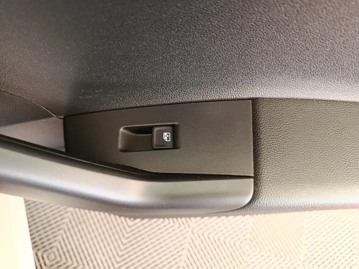 Gros plan sur le bouton de commande de lève-vitre côté conducteur dans l'habitacle noir du Volkswagen Polo gris clair.