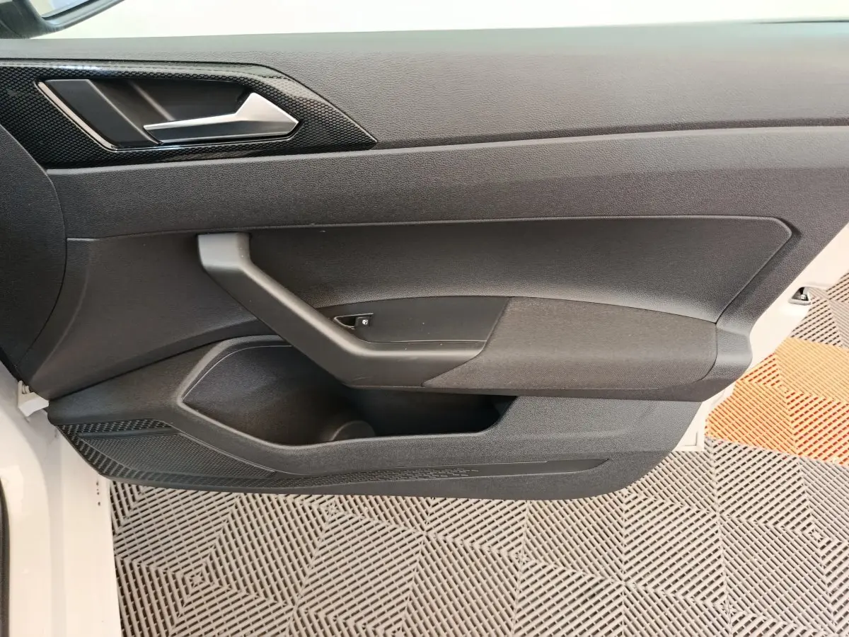 Vue latérale du panneau de porte intérieur gris foncé de la Volkswagen Polo 2023, avec poignée intégrée et rangement.