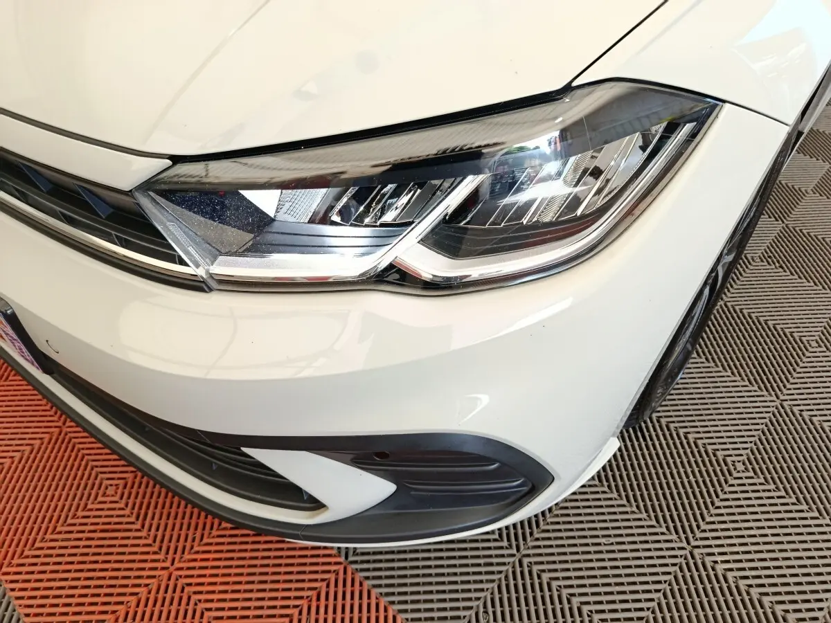 Gros plan sur le phare avant droit de la Volkswagen Polo gris clair, avec détails du pare-chocs et calandre.