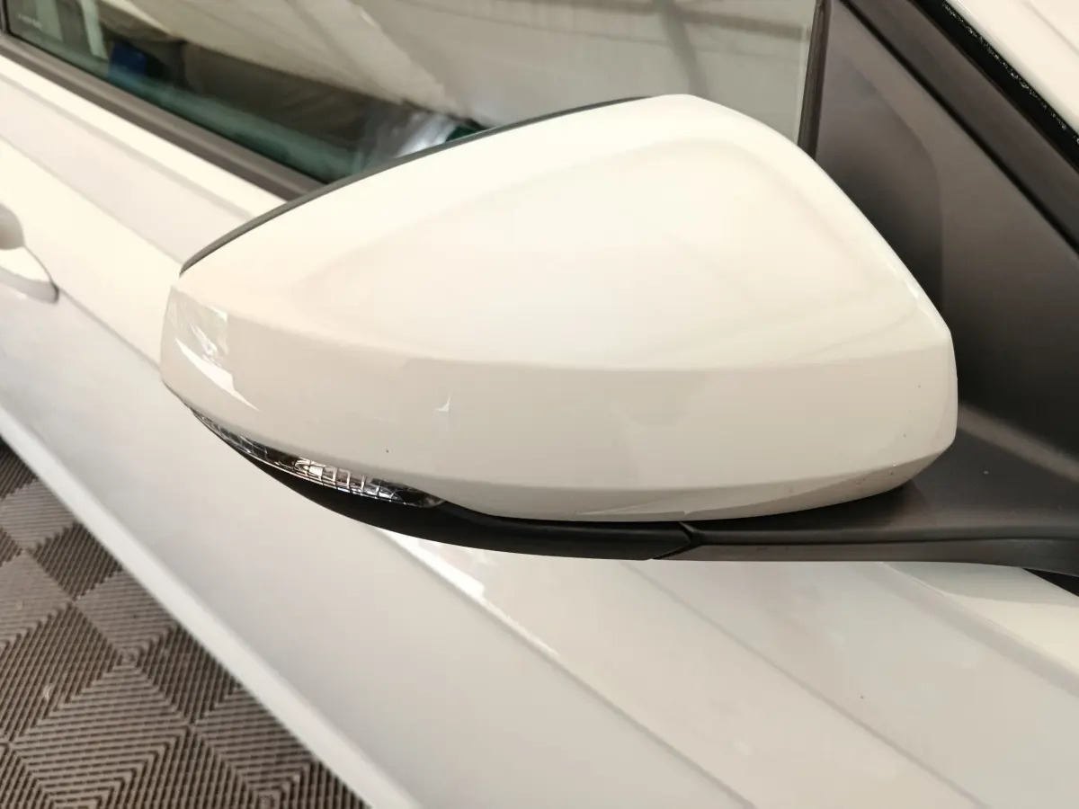 Gros plan sur le rétroviseur droit blanc d'une Volkswagen Polo 2023, avec clignotant intégré et carrosserie claire visible.