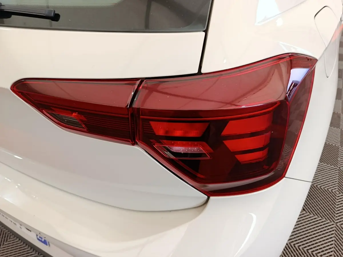 Gros plan sur le feu arrière droit rouge d'une Volkswagen Polo gris clair, avec partie de la carrosserie visible.