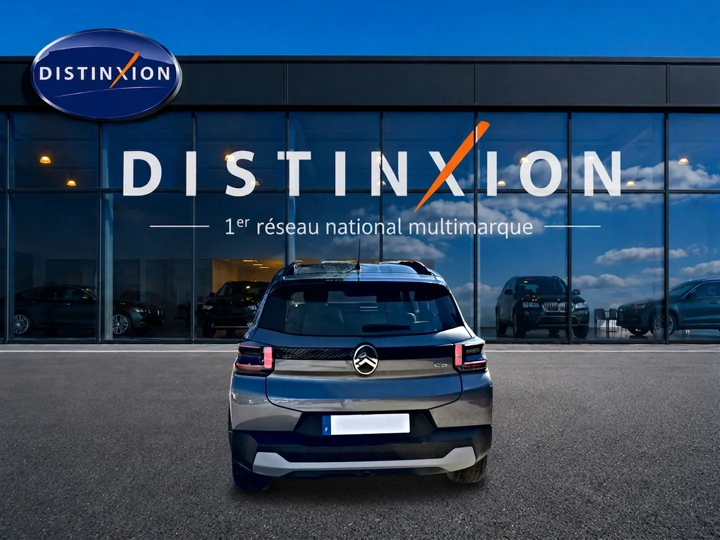 Vue arrière d'une Citroën C3 gris mercure garée devant une vitrine avec logo Distinxion.
