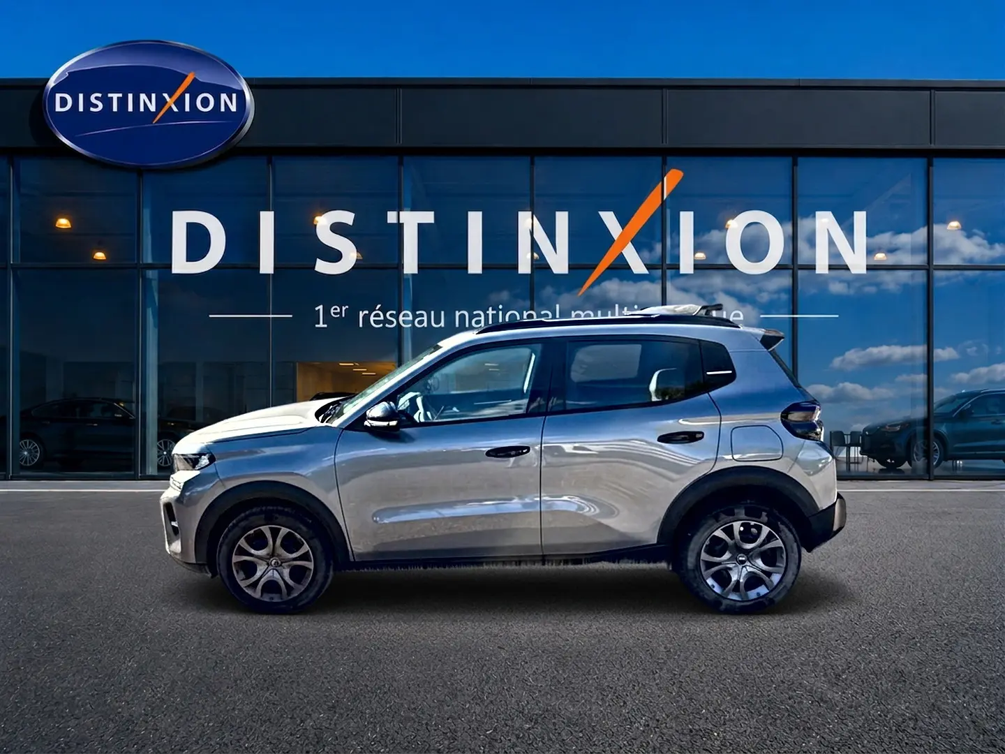 Profil droit d'une Citroën C3 1.2 turbo 100 essence gris mercure avec jantes alu, stationnée devant une vitrine Distinxion.