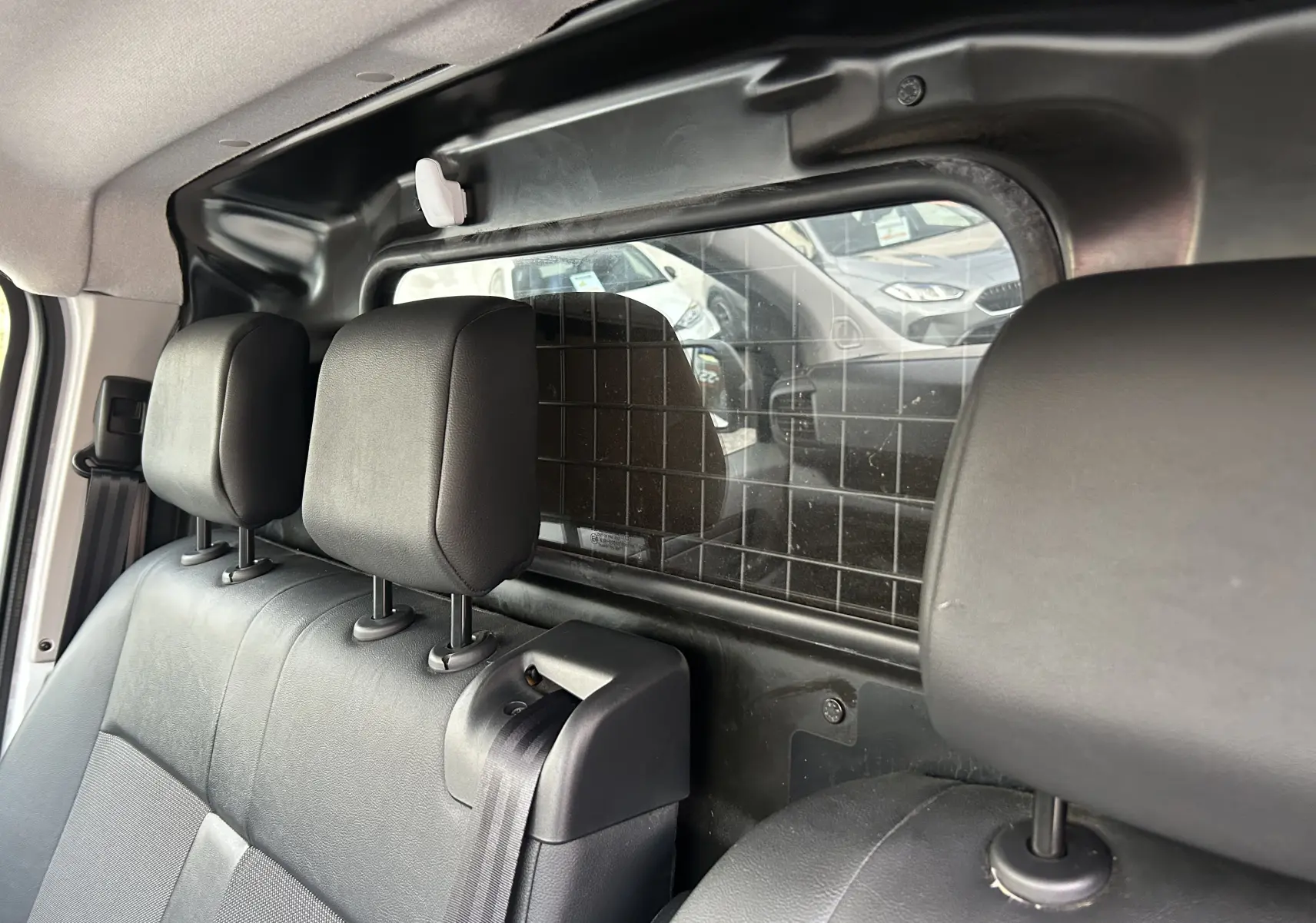 Vue intérieure arrière du Citroën Jumpy blanc, montrant la banquette avec appuie-têtes et séparation grillagée vers le coffre.