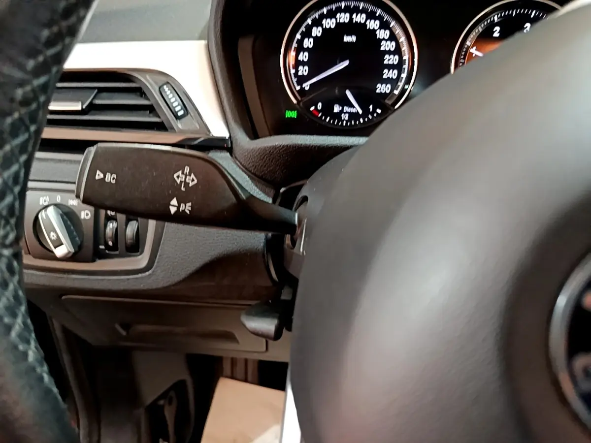 Gros plan sur le volant cuir et le combiné d'instruments du BMW X1 noir, avec commandes et tableau de bord visibles.